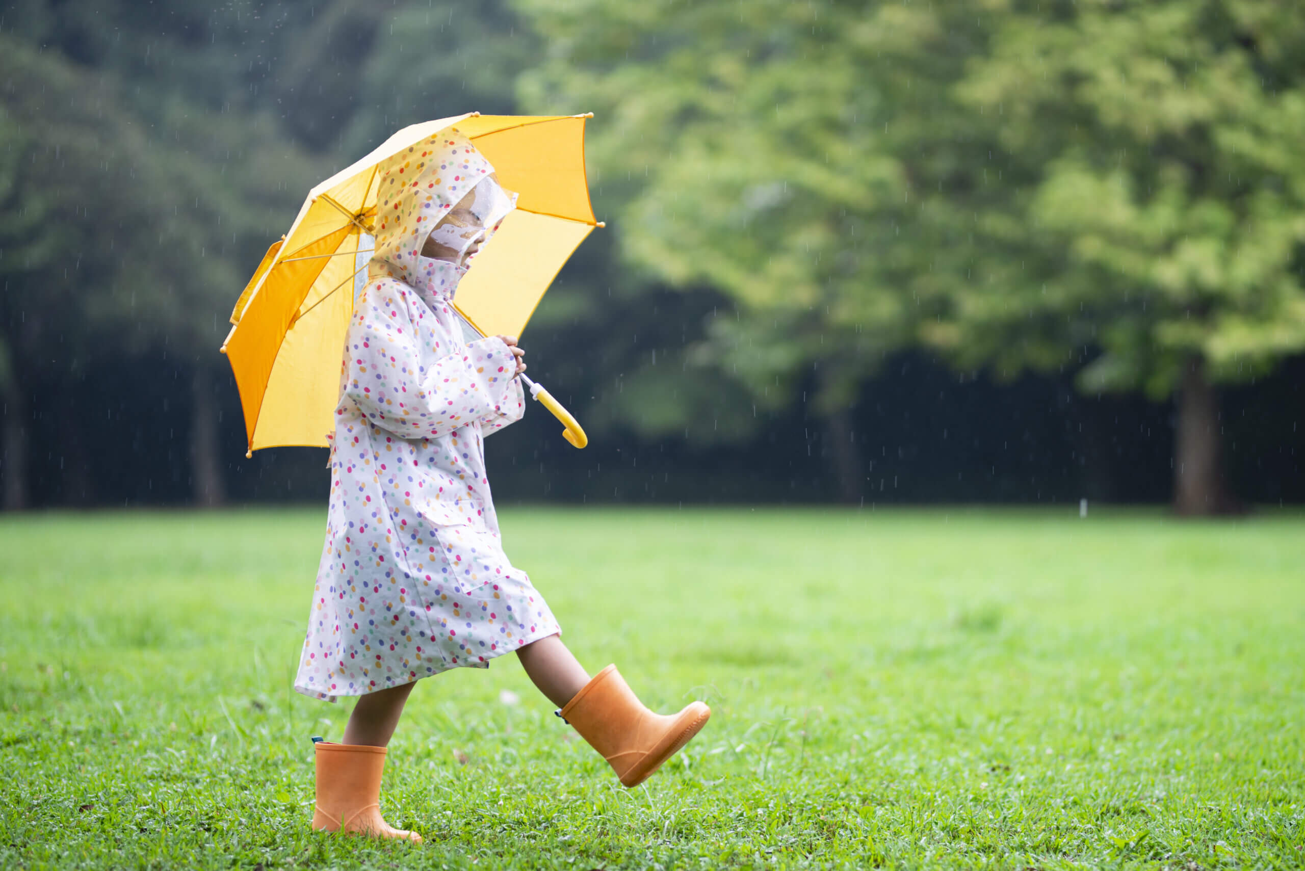 Person standing in the rain walking on grass with umbrella during summer showers.
