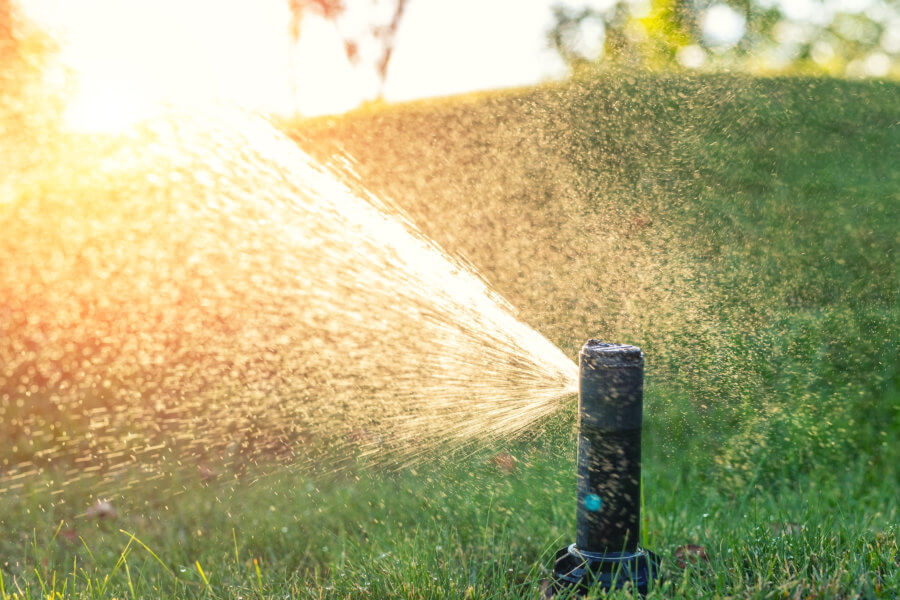 grass maintenance Close-up automatic garden watering system with different sprinklers installed under turf. Landscape design with lawn hills and fruit garden irrigated with smart autonomous sprayers at sunset time.